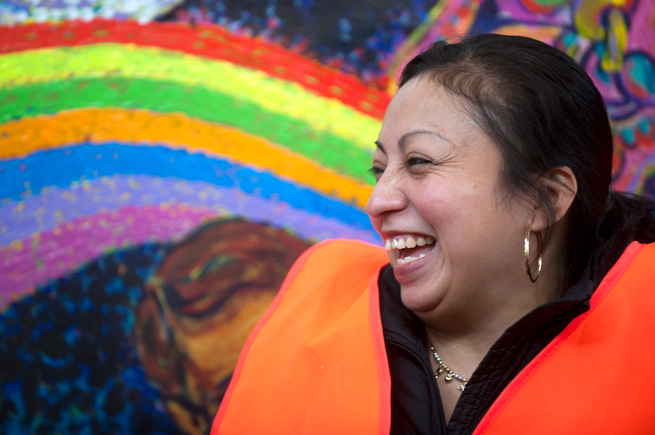 Latina woman with bright orange safety vest in front of a mural